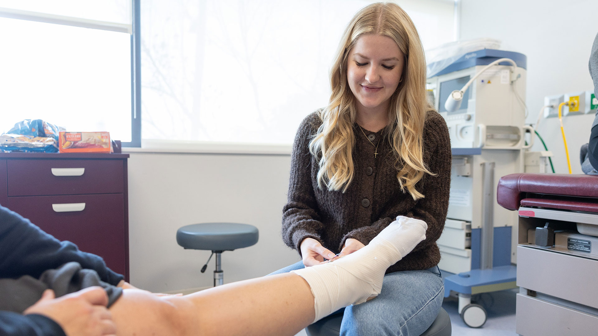 A graduate nursing student uses wrapping to bandage a patient's foot.