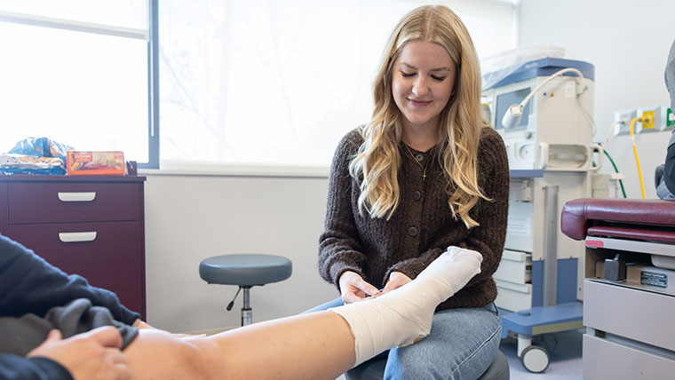 A graduate nursing student uses wrapping to bandage a patient's foot.