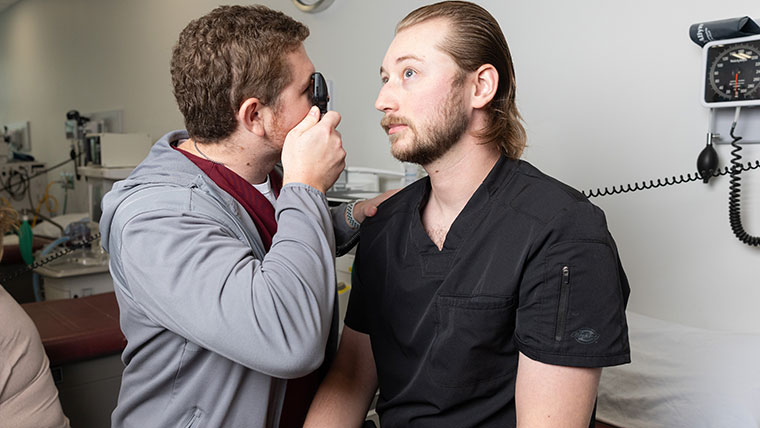 A nursing graduate student performs an eye exam on a classmate.
