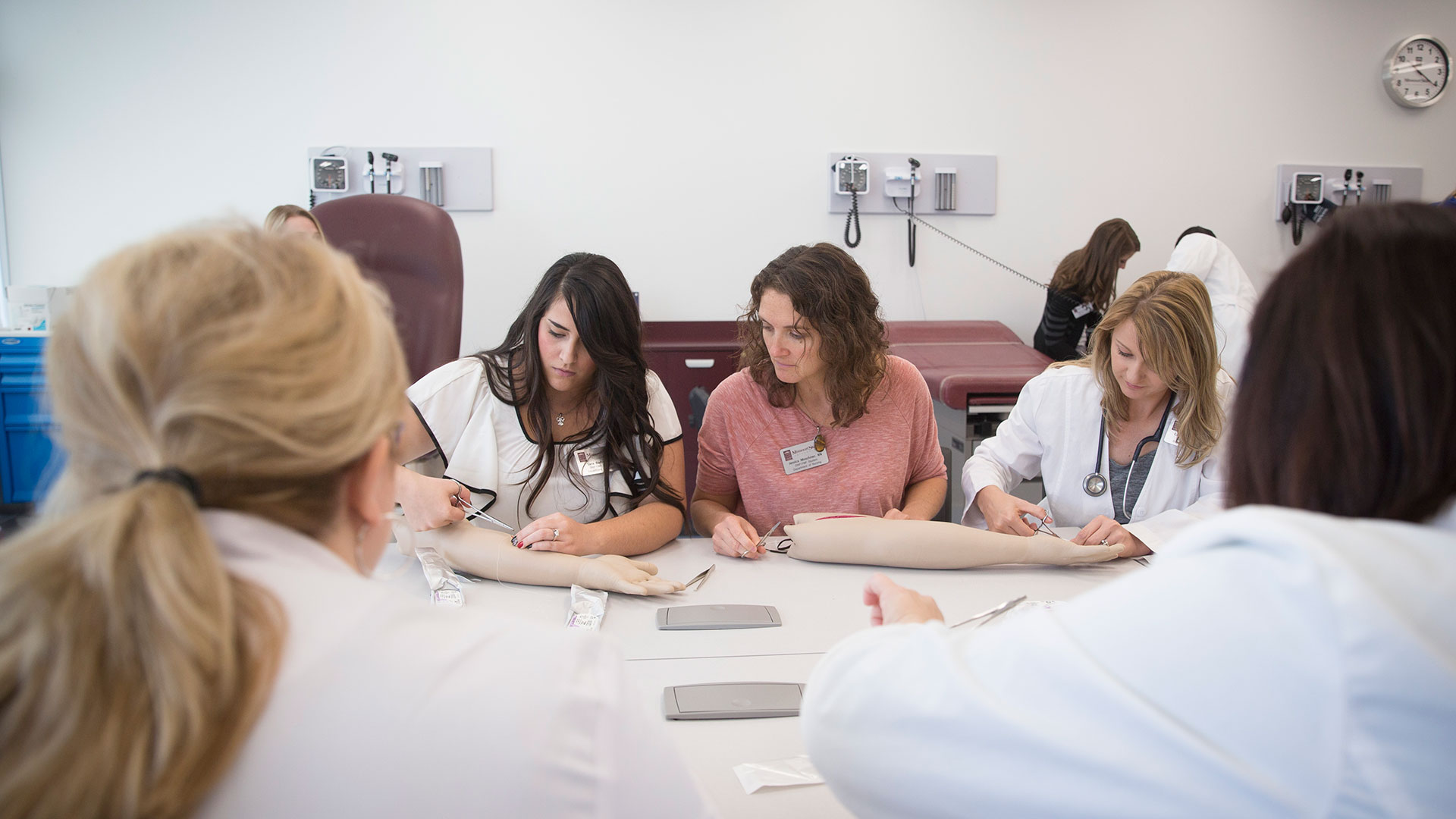 Nursing students practicing putting stitches in a mannequin arm.