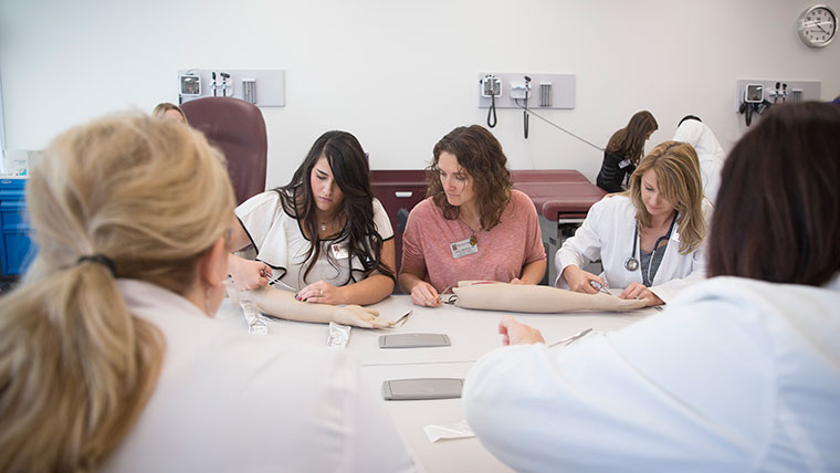 Nursing students practicing putting stitches in a mannequin arm.