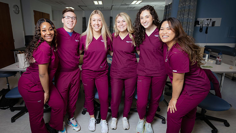 A group of nursing students wearing maroon scrubs in the simulation lab. 