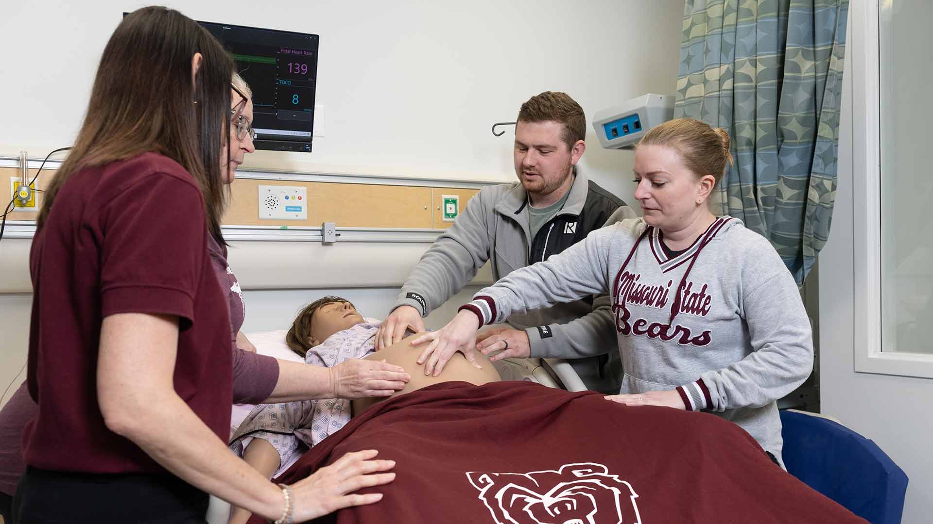 Two nursing students and two professors massage a birthing simulator in the simulation center.