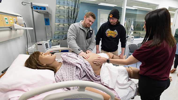 Two graduate students and a professor practice caring for a pregnant mannequin patient.