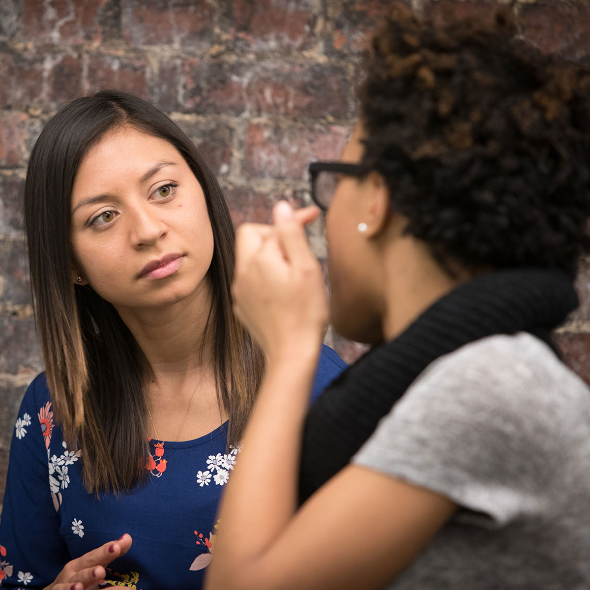 Two women chatting, as one readjusts her glasses.