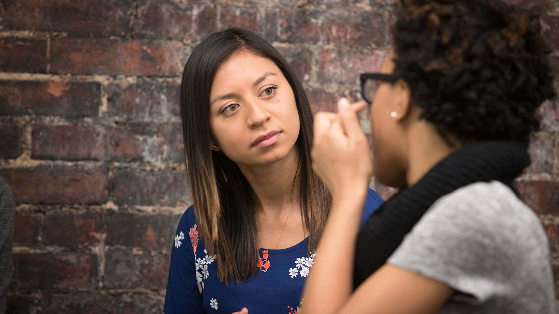 Two women chatting, as one readjusts her glasses.