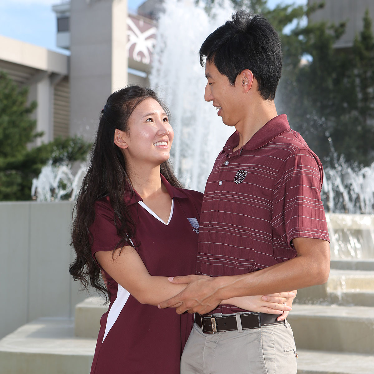 Two married students embrace in front of the campus water fountain.