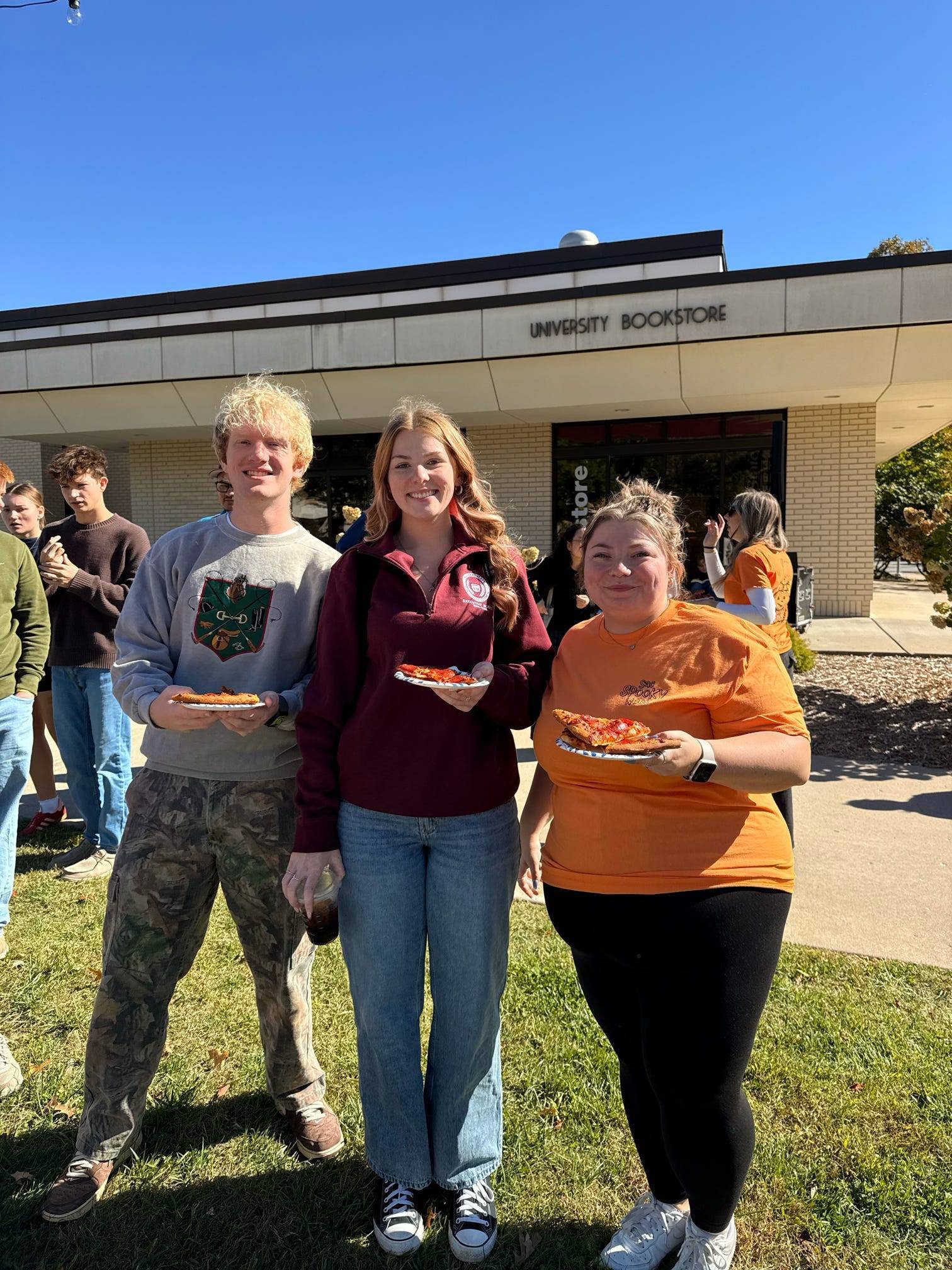 3 students standing side by side holding pizza