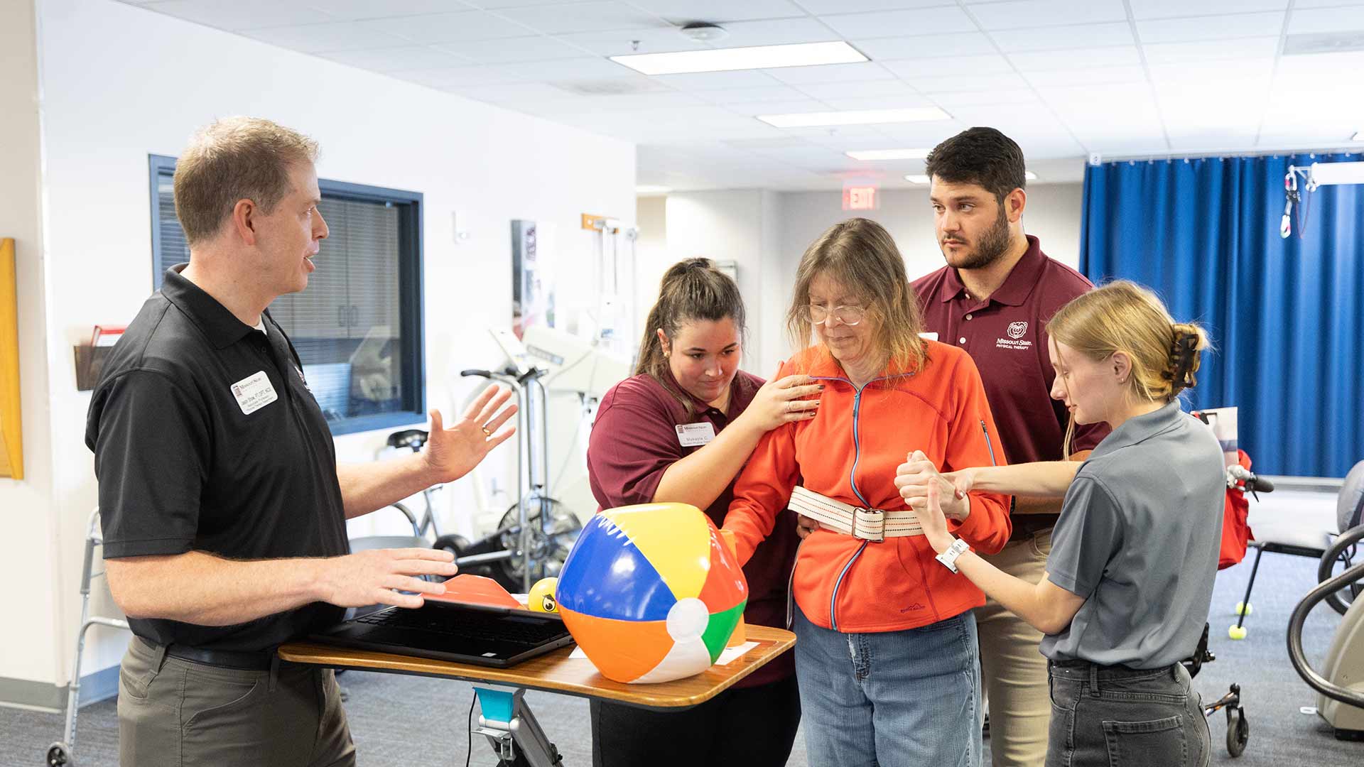 A physical therapy professor provides instruction as three students help a client move around at the Physical Therapy Clinic on campus.
