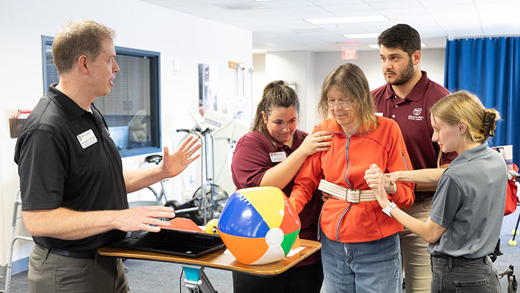 A physical therapy professor provides instruction as three students help a client move around at the Physical Therapy Clinic on campus.