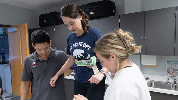 Two physical therapy students helping another student walk in prosthetic footwear.