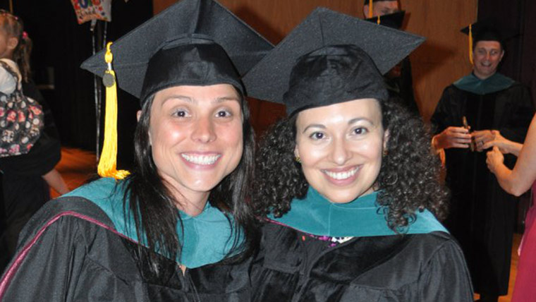 Two Missouri State physical therapy students pose for a photo during a commencement ceremony. Both are wearing black caps and gowns.