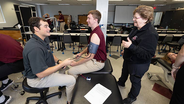 Physical therapy professor Dr. Susan Robinson guides two students through a lab activity.