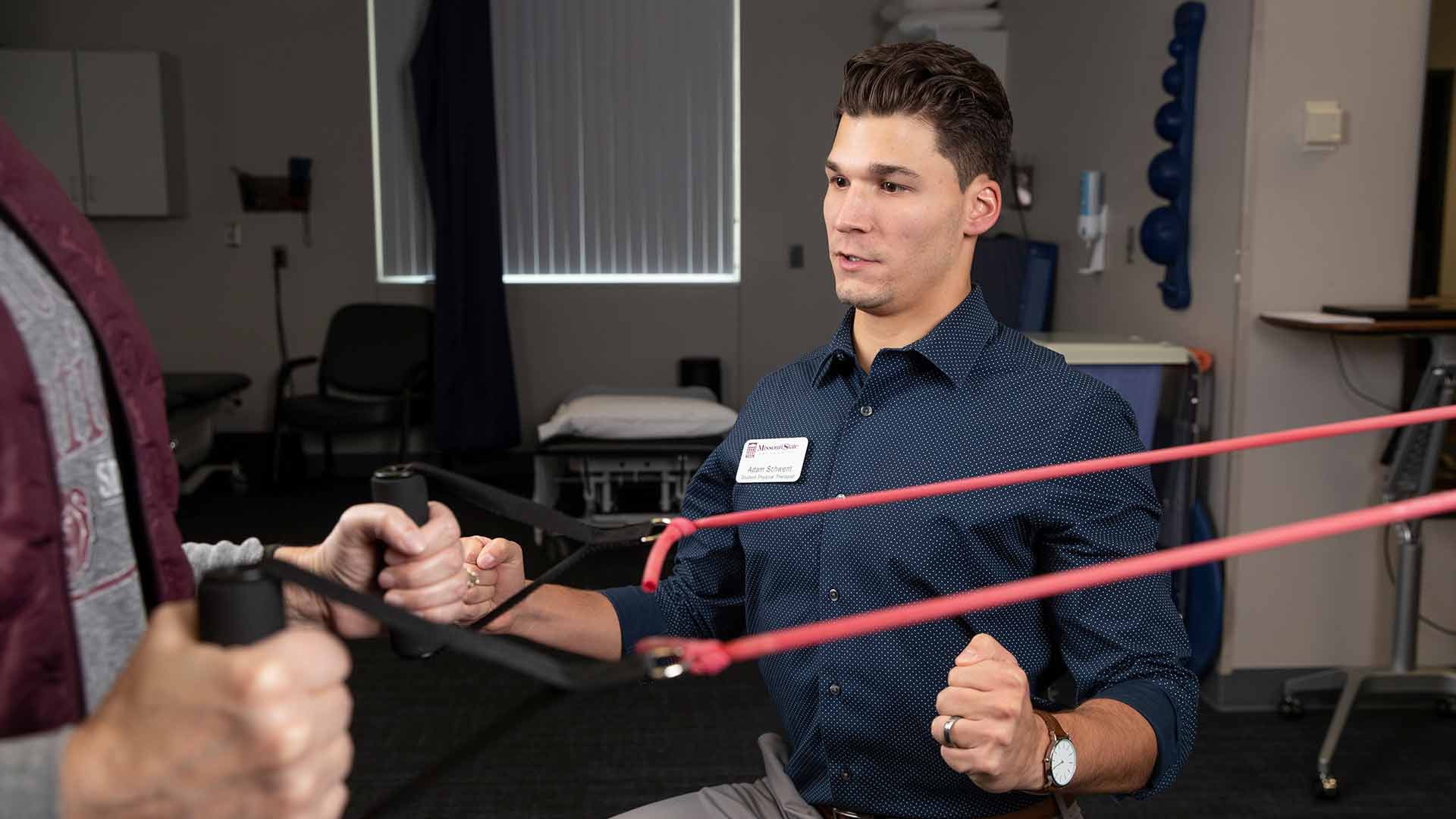 A physical therapy student instructs a client on how to use a pulley machine.