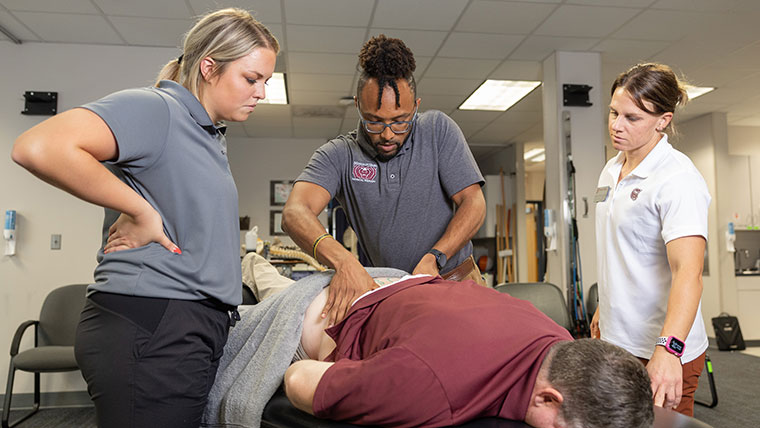 Two physical therapy students and a professor going over spine care techniques on a patient.