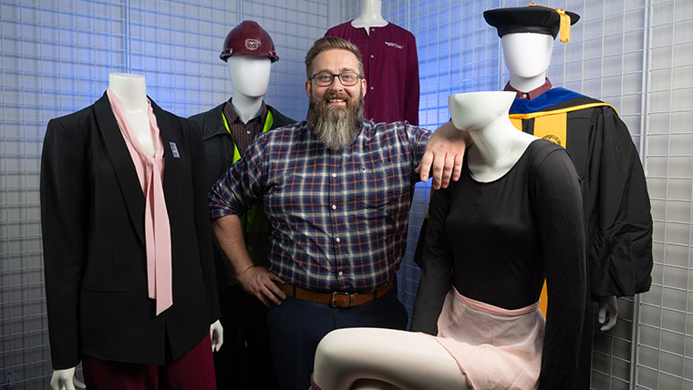 Portrait of Dr. Dan Goering, associate professor in the department of management, as he is surrounded by professionally-dressed mannequins.