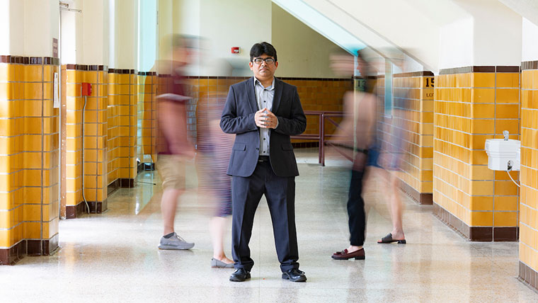 Dr. Muhammad Hassan Raza stands in the center of a hallway, as people blurrily move in the background.