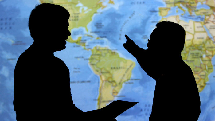 Dark silhouettes of two people standing in front of a world map