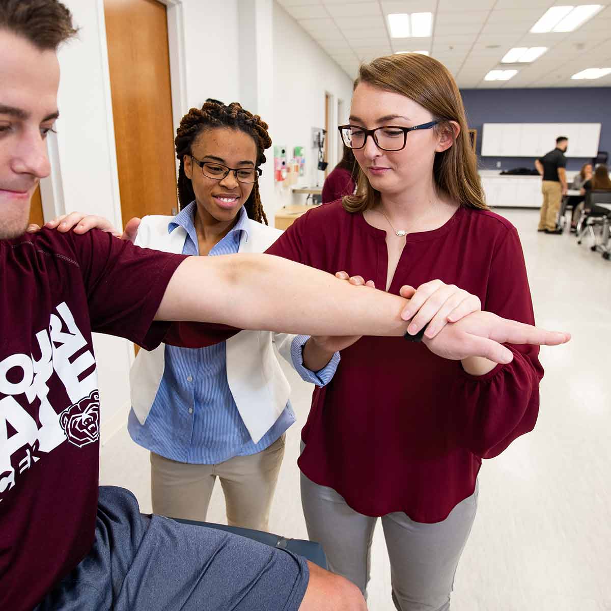An athletic training faculty member supervises another student doing arm tests.