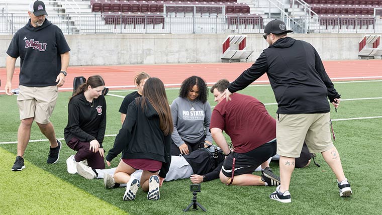 Athletic Training students working on football safety situations as their professors observe.