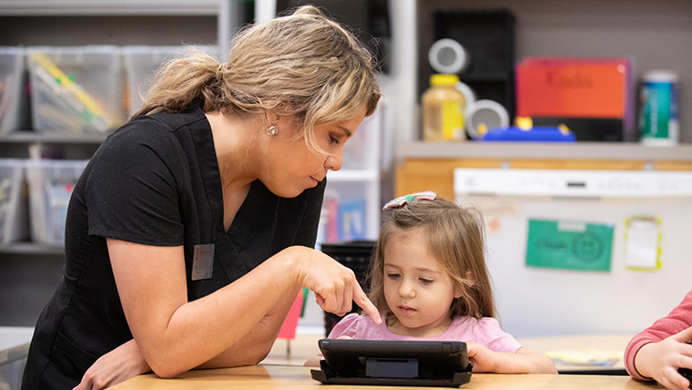 An audiology student does an activity on a table with a young child who has a hearing impairment.