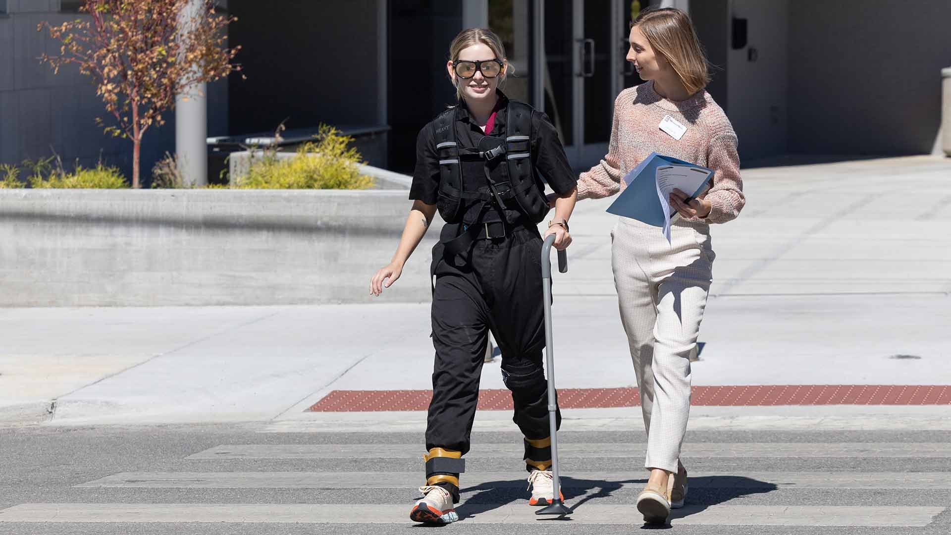 A physical therapy student assists another student across a crosswalk during an old age simulation lab.