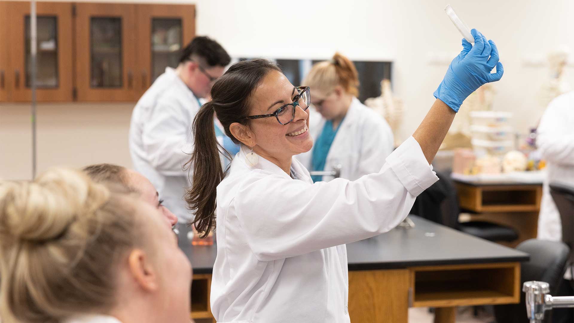 A professor holding up a petri dish in a science lab class.