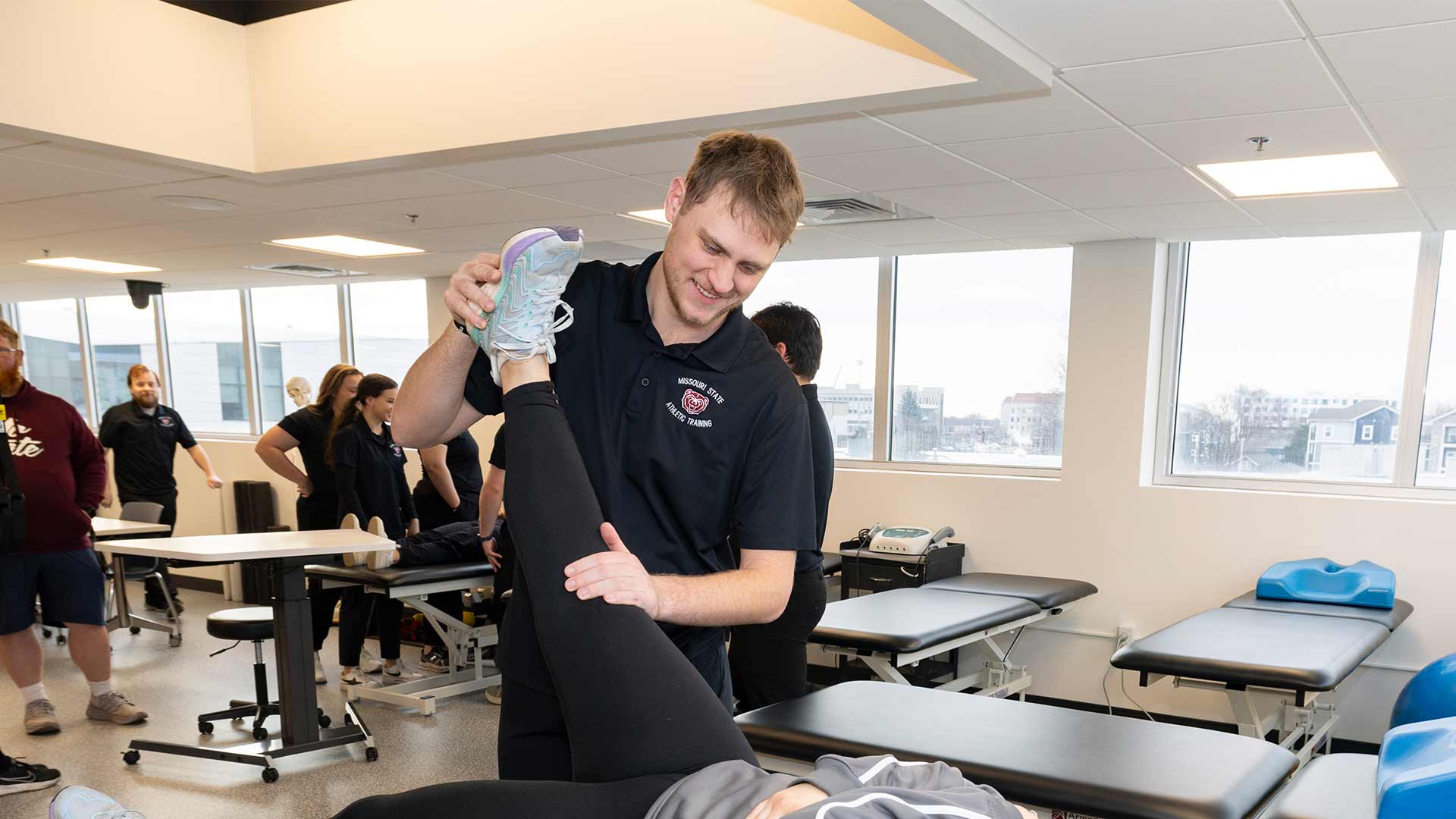 An athletic training student stretches the leg of another student laying on a table.
