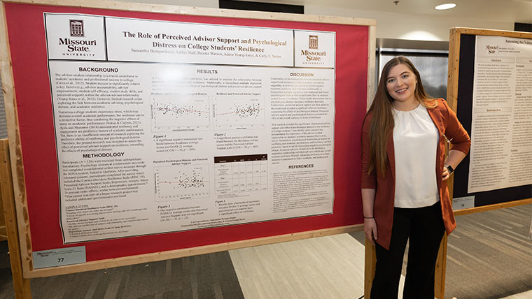 Student posing next to her posterboard at the student research symposium.