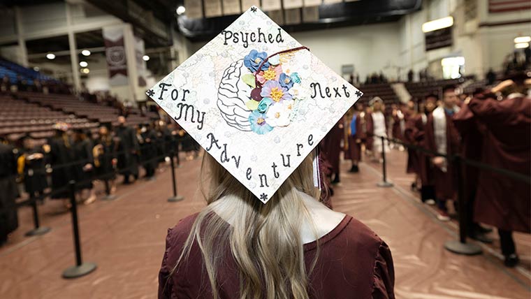 A student's mortarboard at commencement with the message, "Psyched for my next adventure" written decoratively.