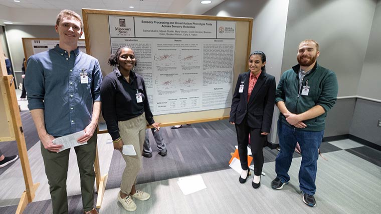 A group of psychology students pose in front of their research poster at the Student Research Symposium.