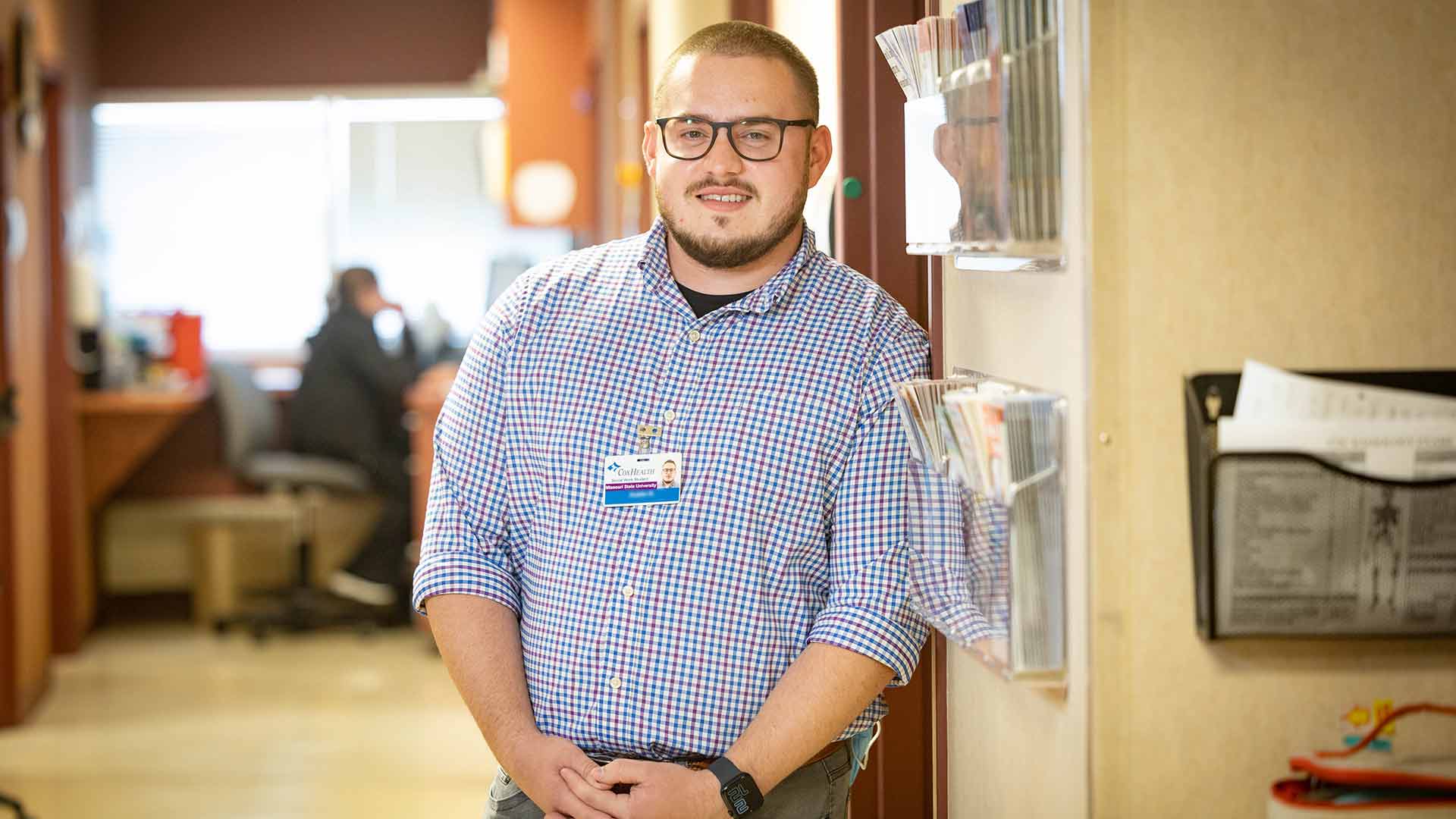 A Master of Social Work student poses in the hallway of a health clinic, where he's completing his practicum.