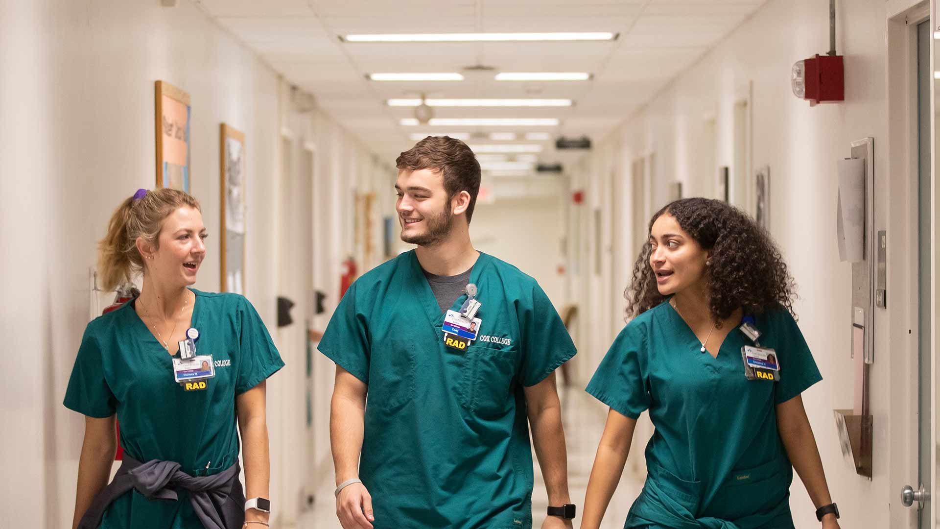 Three students talking and walking down a hallway.