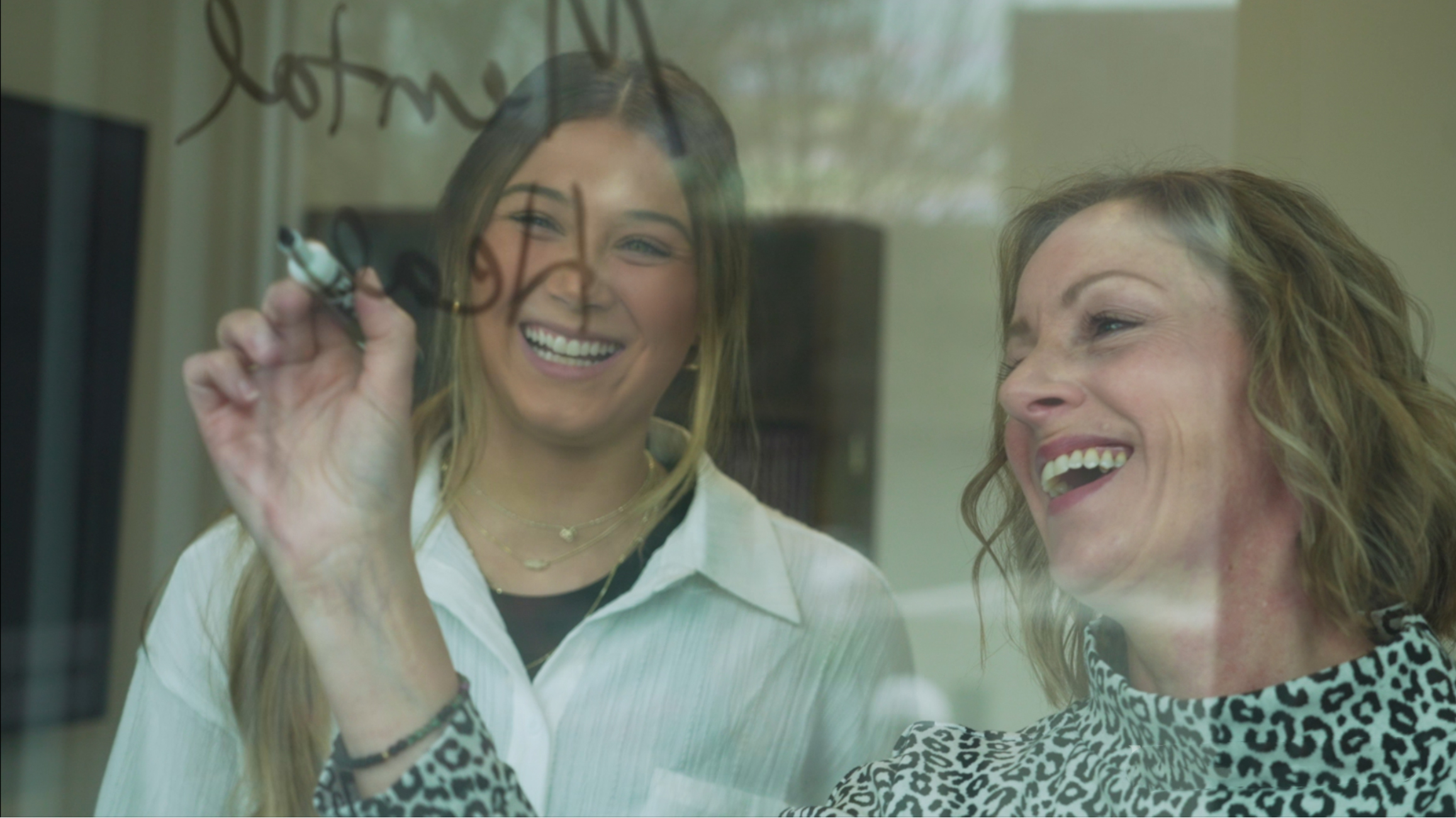 A faculty member illustrates something to a student on a window with dry erase marker