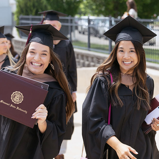 Two Missouri State students in cap and gown holding their diploma covers.