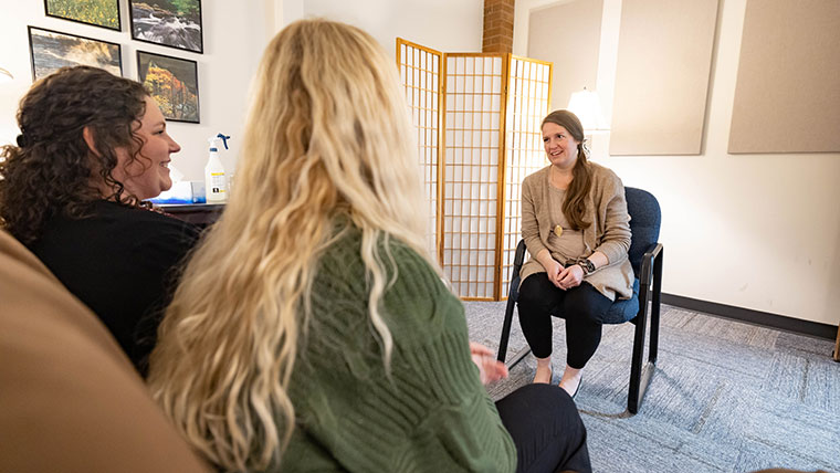 Two clients seated on a couch chat with a counselor.