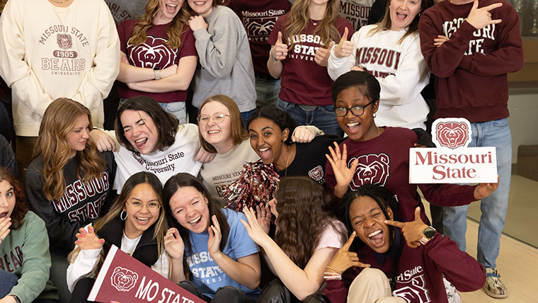 A group of students pose with Missouri State banners and merchandise during SOAR.