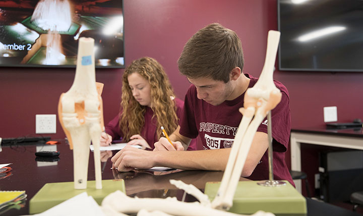 Two students in a biomedical science class jot down notes.