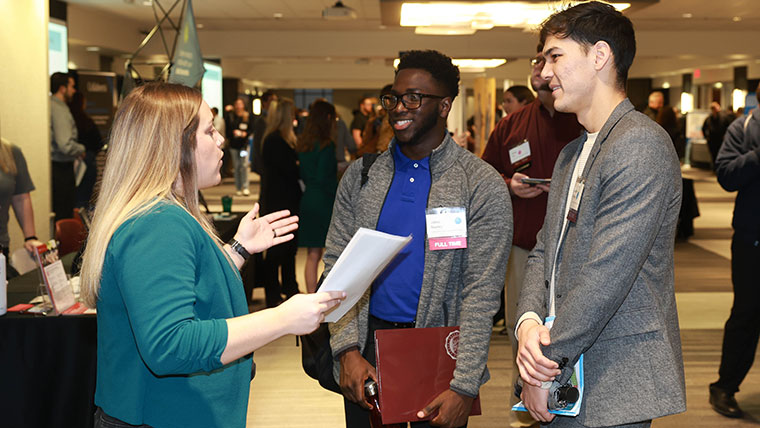 A businesswoman discusses job opportunities with two students during a Career Fair.