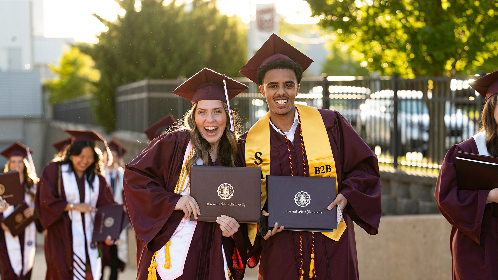 Two smiling Missouri State graduates hold their diplomas after the commencement cermony.