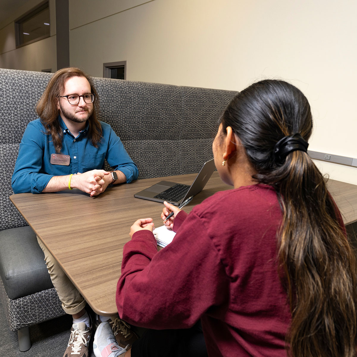 Jack Baumgart, a student success coach, gives guidance to a student who is writing in a notebook.