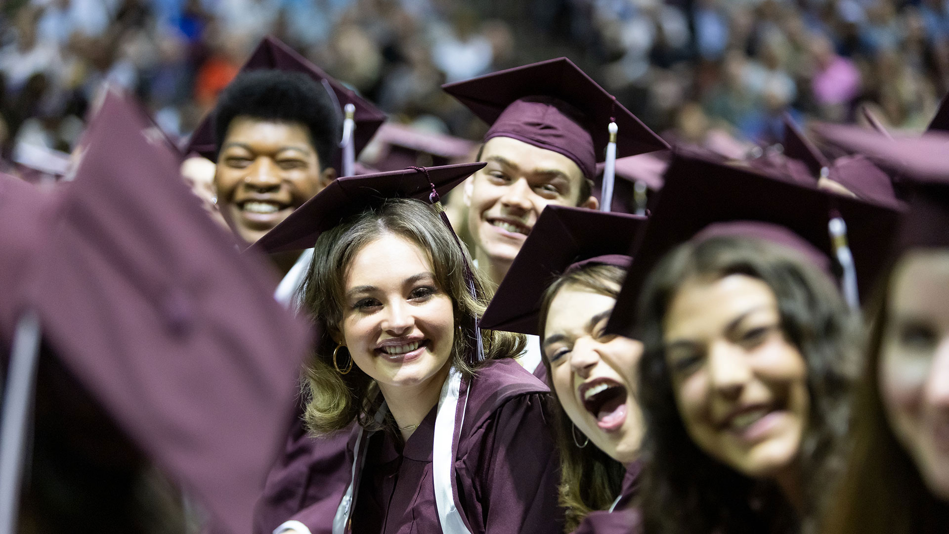 A row of at least five graduates smile excitedly during their commencement ceremony.