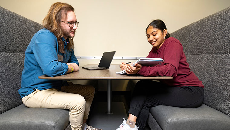 Jack Baumgart, a student success coach, sits across the table from a student who shows him a notebook with her academic plans.