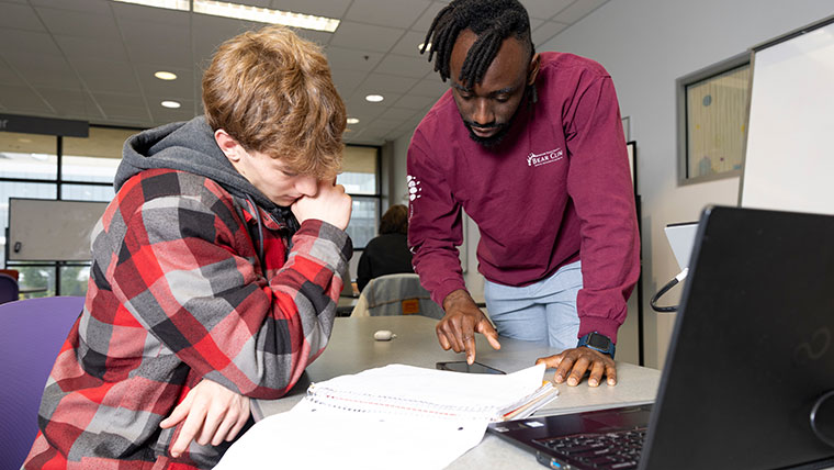A student listens as a tutor in the Bear CLAW explains a math concept to him from his notebook.