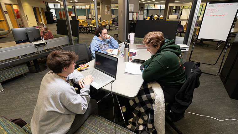 Three students using laptops and notebooks to study in the Writing Center at Meyer Library.