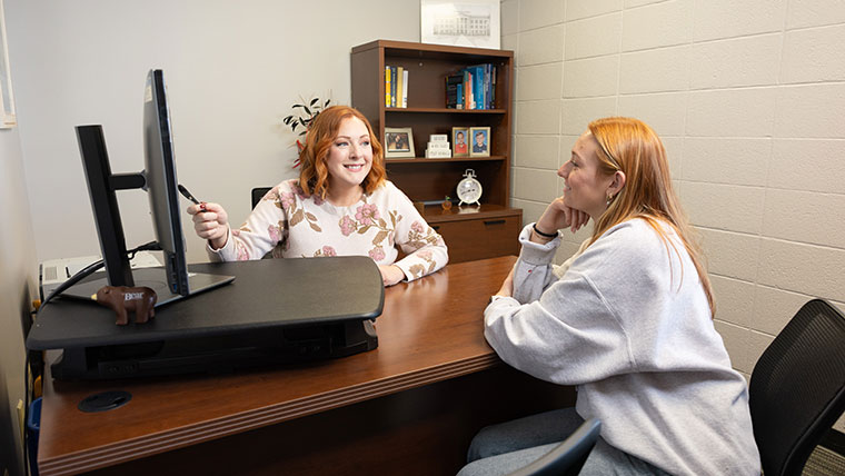 An advisor shows her advisee a list of course options for registration on her office computer during an advising session in University Hall.