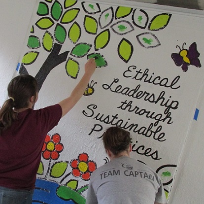 Two students painting a mural stating 'ethical leadership through sustainable policies'.