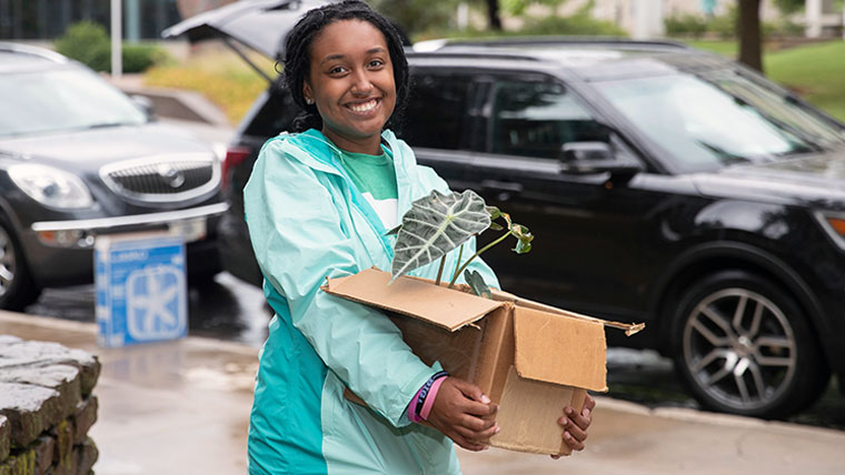 Missouri State student carrying a plant in a box on campus. 