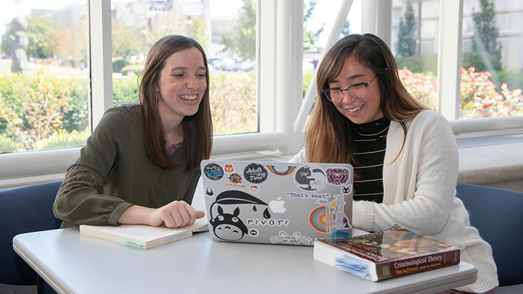 Two smiling Missouri State students sitting within the Meyer library at a laptop. 