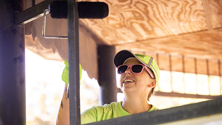 A Day of Caring volunteer uses a paint roller to apply a fresh coat to an outdoor gazebo.